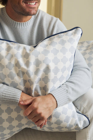 A person wearing a light gray sweater sits on a sofa, smiling and holding the Oversized Mod Dot Grid Pillow, which features a hand-drawn pattern. Only their hands and lower face are shown, showcasing modern Southern decor style.