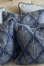Several Oversized Mod Palm Pillows in navy blue with a white palm leaf pattern are arranged on a light couch, making them ideal for bringing a touch of Southern style to your home decor.