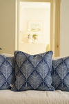 Three Oversized Mod Palm Pillows in navy blue with white leaf patterns are placed on a light sofa. Through the doorway, a bright room featuring Southern-style decor can be seen in the background.