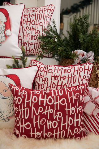 The Ho Ho Ho Lumbar Pillow, featuring festive Santa Claus faces, rests on a cozy surface surrounded by greenery, wrapped gifts, and holiday decorations—creating the perfect holiday accent.