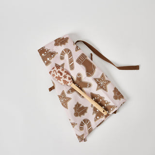 A folded apron with a gingerbread cookie pattern and brown straps sits next to the Pink Gingerbread Spatula, both featuring festive holiday cookie designs and displayed on a white background.