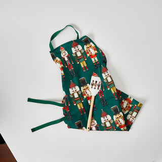 A festive green apron with colorful nutcracker designs and a matching white BPA-free silicone Nutcracker Spatula—an ideal holiday baking gift for any kitchen.