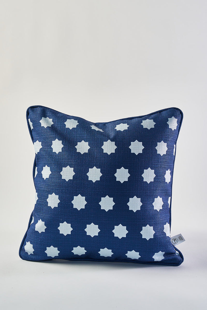 The Mod Stars Pillow is square and navy blue with evenly spaced white star shapes. It features a small fabric tag on the right side and is shown against a plain white background.