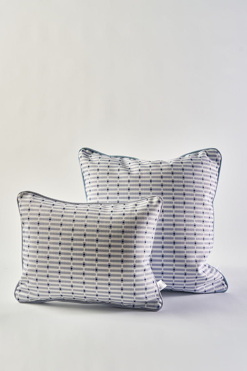 Two white accent pillows inspired by the Mod Mini Crossing Tiles Lumbar Pillow, featuring blue and black geometric dot and line patterns with blue piping, are placed together on a plain white background. The larger pillow sits slightly behind the smaller one.