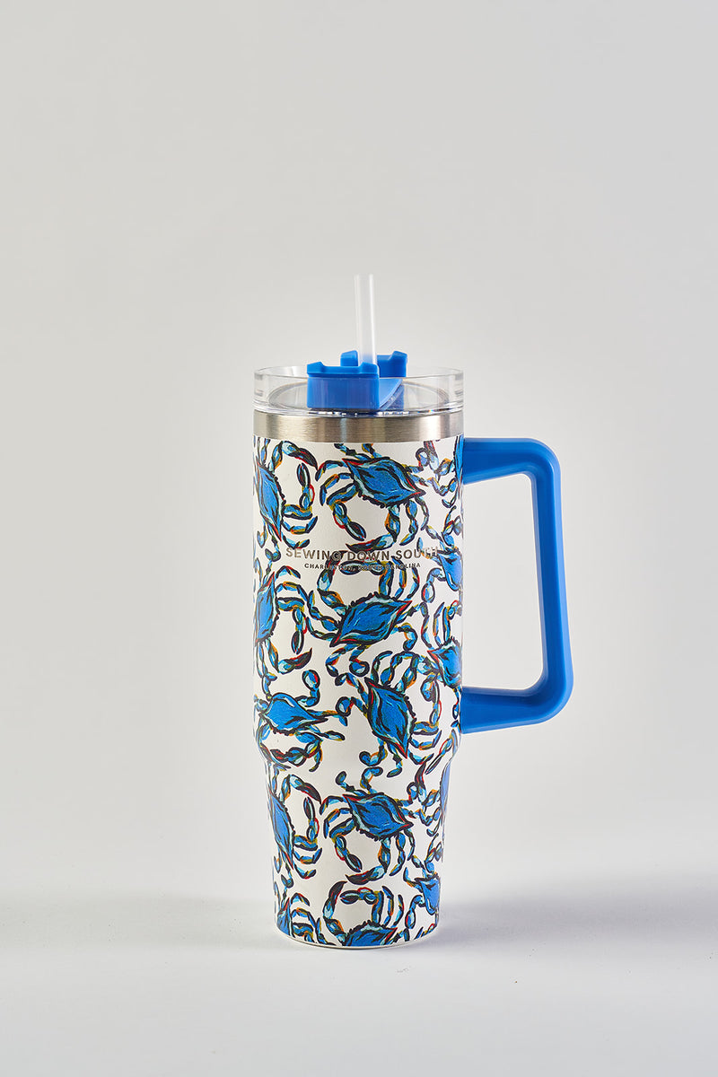 The Crab Craze 30oz Tumbler is a large white stainless steel cup featuring blue crabs, a blue handle, blue lid, clear straw, and a no sweat exterior. The insulated drinkware is shown on a plain white background.