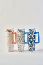 Three Crab Craze 30oz stainless steel tumblers with large handles, lids, and straws—each with a unique blue and orange geometric or abstract design—are displayed together. The insulated build keeps drinks cold and the exterior dry.