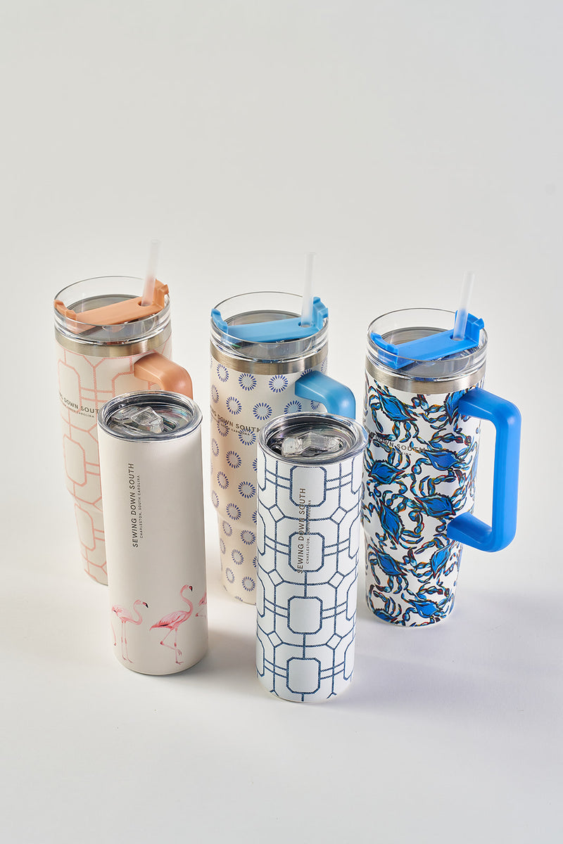 Five Crab Craze 30oz Tumblers, each with unique patterns—geometric, blue handles, and pink flamingos—are arranged on a white surface. Made of stainless steel, these insulated cups come with straws and a no-sweat exterior.