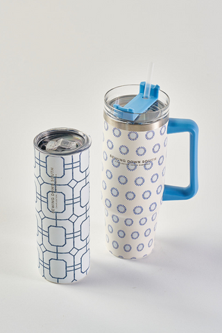 Two white travel mugs with blue geometric patterns; one has a blue handle and straw lid with sunburst designs, the other is taller with a clear lid and square lattice pattern.