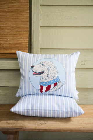 A Loyal Liberty Lumbar Pillow featuring blue and white stripes and a dog in a patriotic scarf rests on a matching pillow atop a wooden bench, adding charming, garden-inspired decor to the space.