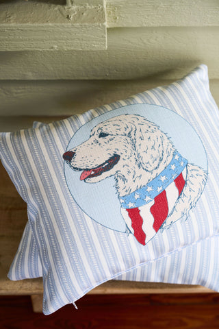The Loyal Liberty Lumbar Pillow showcases a white dog in a star and stripe scarf resting on a matching cushion, bringing charming garden-inspired decor to your space.
