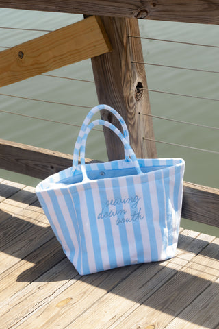 The Weekend Getaway Stripe Terry Tote, featuring blue and white stripes and “Sewing Down South” embroidered on the front, sits on a wooden dock by the water—perfect for your next getaway.