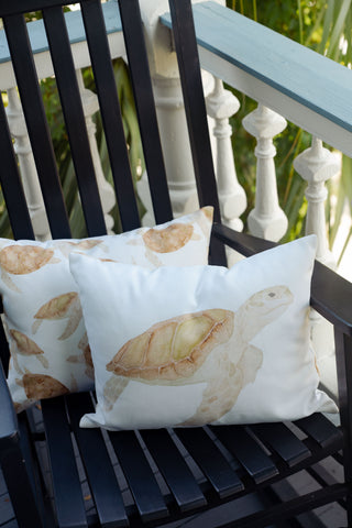 The Outdoor Tidal Travelers Lumbar Pillow adds a charming coastal accent to your space, shown here resting on a black wooden chair on an outdoor balcony with white railings and lush green foliage in the background.