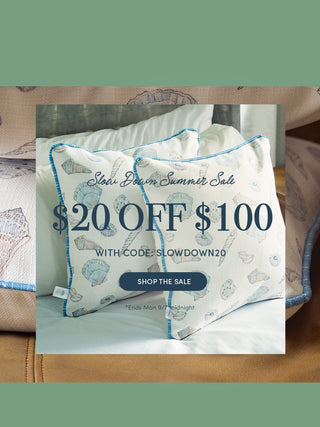 Promotional banner for a slow swim summer set, featuring a large close-up of a beige pillow with a blue seashell pattern and text reading '$20 OFF $100 WITH CODE: SLOWDOWN20' alongside a smaller inset photo of two matching patterned pillows on a bed.