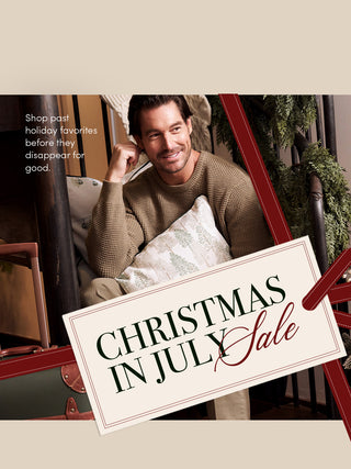 A promotional banner featuring a smiling man in a knit sweater sitting in a chair with a pillow, overlaid with the text 'Shop past holiday favorites before they disappear for good.' and a large tilted sign reading 'CHRISTMAS IN JULY Sale.