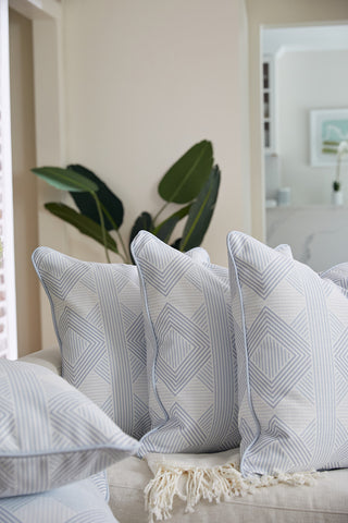 Four Oversized Mod Geo Diamond Pillows with light blue geometric designs sit on a beige couch. A cream fringe throw and green plants add brightness, creating a stylish space inspired by Sewing Down South.