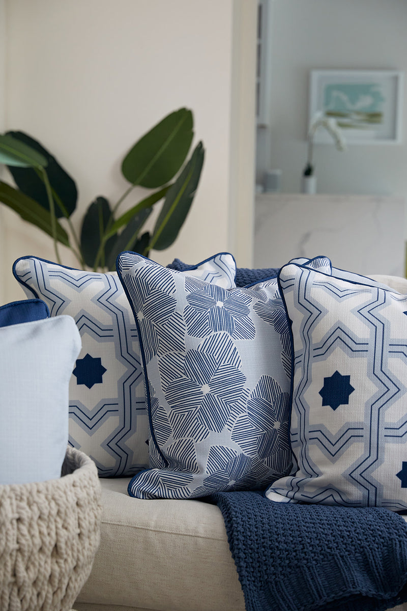 A cozy living room features a neutral couch with decorative pillows, including the Mod Flora Pillow from the Modern Collection showcasing an exclusive Sewing Down South™ pattern. A knitted blanket adds warmth, while greenery and framed artwork enhance the modern flair.