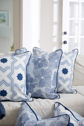 The bright, sunlit room features four decorator pillows on a light sofa, including the Oversized Mod Stella Tile Pillow in blue twill with a bold geometric pattern, set against white walls and a glass-paned door.