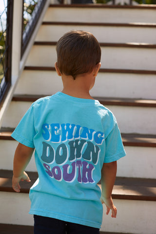 A child with short brown hair, wearing the Youth SDS Bubble Tee, stands at the bottom of outdoor wooden stairs and faces away from the camera.