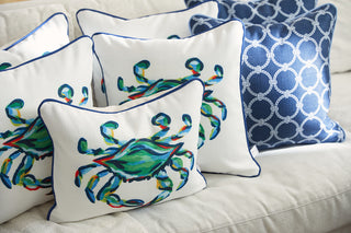 A cozy Coastal Collection display features The King Crab Lumbar Pillow with Navy, adorned with vibrant designs and blue piping, alongside a Navy Rope Rounds Pillow with a striking white geometric circular pattern.