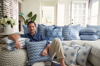 A person sits on a sofa with Navy Starburst Pillows, surrounded by blue and white patterns in a bright room. A brick wall and potted plant in the background enhance the cozy charm, reflecting Sewing Down Souths style.