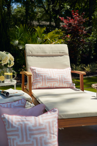 A chair with a Coral Greek Key Extended Lumbar Outdoor Pillow and a magazine rests on a table, featuring SDS Shield® Outdoor Fabric for lasting style and comfort.