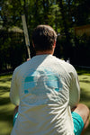 Wearing a Charleston Pineapple Crewneck showcasing the famous pineapple fountain, this individual holds a croquet mallet on a green lawn bordered by trees and a rustic fence.