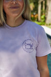 A person wears an Orchid WWWMS Short Sleeve Tee with a vintage sewing machine design, made from 100% ring spun cotton. The text reads SEWING DOWN SOUTH, EST 2019, CHARLESTON, SOUTH CAROLINA, set against an outdoor backdrop with trees.