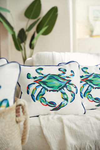 The cozy living room features a white sofa with decorative pillows from the Coastal Collection, including The King Crab Lumbar Pillow with Navy. A woven basket and a tall green plant add natural touches to complement the colorful crab design.