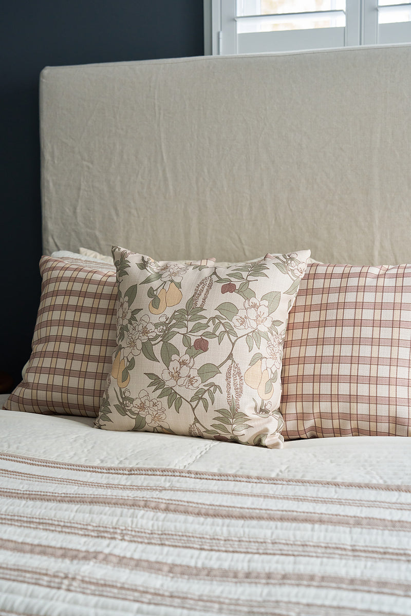 A neatly made bed features two plaid pillows and a Fall Florals Pillow in front, all in neutral tones. A beige headboard and sunlight streaming through white shutters complete the cozy, inviting scene.