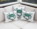 Three Outdoor King Crab Lumbar Pillows with navy accents, crafted from SDS Shield® Outdoor Fabric, adorn a beige sofa on a patio. The setting is completed by a black fence backdrop, creating a coastal-themed ambiance.