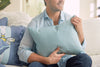 A person in a light blue shirt sits on a sofa with a Bee & Florals Collection: Bee Trio Lumbar Pillow. The calm, cozy setting with soft lighting enhances the scenes charm. This USA-crafted pillow by Sewing Down South adds warmth to the ambiance.