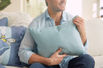 A person in a light blue shirt sits on a sofa with a Bee & Florals Collection: Bee Trio Lumbar Pillow. The calm, cozy setting with soft lighting enhances the scenes charm. This USA-crafted pillow by Sewing Down South adds warmth to the ambiance.