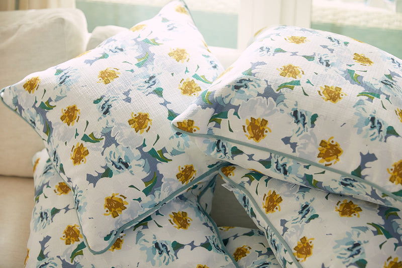 Blossoming Peonies Pillows from the Bee & Florals Collection are artfully arranged on a light couch. Their blue, green, and yellow floral print adds elegance and charm with Sewing Down South® craftsmanship as natural light streams in from a nearby window.