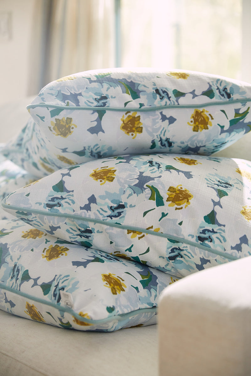 Three cushions from the Bee & Florals Collection: Blossoming Peonies Pillow by Sewing Down South® adorn a light sofa, featuring blue, white, and yellow flowers with green leaves on a soft natural light background.