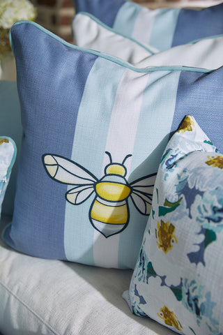 A close-up of decorative pillows on a couch shows the Bee & Florals Collection: Bee Stripe Pillow from Sewing Down South, featuring blue and white stripes with a yellow bee design. The other pillow displays a floral pattern in blue, green, and yellow tones.