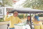 Three people sit in a golf cart on a suburban street. A man in a yellow hoodie chats with two women—one wearing a Charleston Dad Cap, Maroon and the other in a blue cap with an adjustable backstrap. Trees and a house form the perfect backdrop to their conversation.