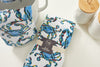 The Crab Craze Kitchen Towels, 2 pack, showcases a vibrant crab design alongside a chic white jar and textured container with a wooden lid. A pot glimpse adds charm, making it perfect for Coastal Kitchen Decor.