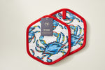 The Crab Craze pot holders, featuring two hexagonal pieces with a vibrant blue crab design and red trim, are perfect for enthusiasts. One has a Pot Holder tag with care instructions. With silicone grip and heat resistance, they are both functional and stylish against a plain light surface.