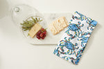 A marble serving board elegantly displays cheese, grapes, and green leaves. A rectangular cracker complements the scene, while a neatly folded Crab Craze Kitchen Towel from a 2-pack set with blue and green designs adds a touch of color beside the board.