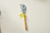 The SDS Spatulas feature a wooden handle and a paisley-patterned blue and white heat-resistant silicone head, tied with a yellow ribbon and elegantly placed on a light surface.
