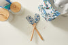 On a flour-dusted countertop, two crossed SDS Spatulas with wooden handles and blue crabs rest among nonstick cookware. Nearby are jars with wooden lids, a patterned towel, and mixer parts—ideal for any culinary adventure!.
