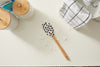 An SDS Spatula featuring a black-and-white speckled design rests on a flour-dusted white surface. Made from heat-resistant silicone, its accompanied by a checkered cloth, a tin of baking powder, and two wooden-topped lidded containers.