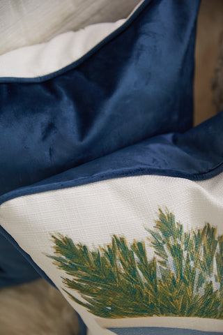The Sleigh Pillow, featuring a white cover with a green botanical print and blue border, is arranged closely with a blue velvet pillow from Sewing Down South for a decorative touch.