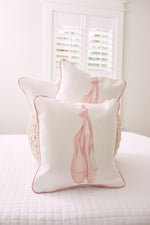 Three white pillows from the Kids Collection, featuring pink piping and ballet shoe illustrations, are stacked neatly on a white quilted bed. The Bow & Ballet pillow by Sewing Down South® catches soft light streaming in through the window with its distinct pattern and design.