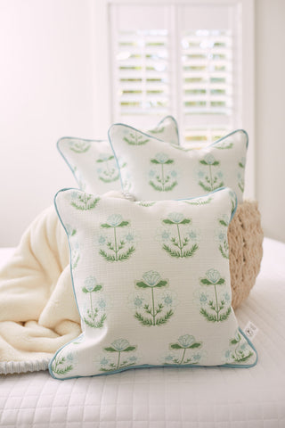 Four Kids Collection: Victorian Floral in Blue pillows are neatly arranged on a white bed, accompanied by a beige blanket. Soft daylight filters through white window shutters in the background, enhancing the vintage charm.