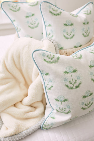 A Kids Collection pillow exhibits Victorian floral patterns in blue and green, elegantly detailed with light blue piping. Paired with a soft beige blanket on a white surface, it adds charm to any room.