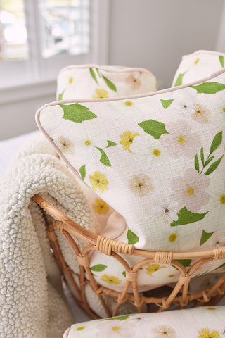 A wicker basket holds a Kids Collection Pink Floral Pillow with green leaves and yellow flowers, paired with a cream sherpa blanket. A softly blurred window casts gentle light on this Sewing Down South® creation.