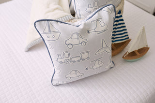 The Kids Collection: Transportation Pillow showcases blue outlines of cars, planes, boats, and trains on a white quilted bedspread. Behind it sits a plush toy in a striped outfit and a decorative sailboat on the bed, enhanced by the charm of its Sewing Down South® pattern.
