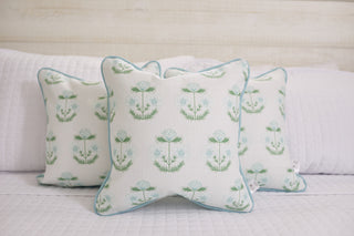 Three Kids Collection: Victorian Floral in Blue Pillows, featuring light blue Victorian floral patterns and blue edges, are displayed on a white quilted bed. Their subtle design complements the soft, neutral bedroom decor beautifully.