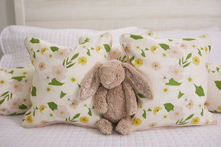 A plush bunny sits surrounded by the Sewing Down South® Kids Collection, featuring Pink Floral Pillow adorned with green leaves and flowers. It rests on a white quilted bedspread, creating a cozy and inviting atmosphere.